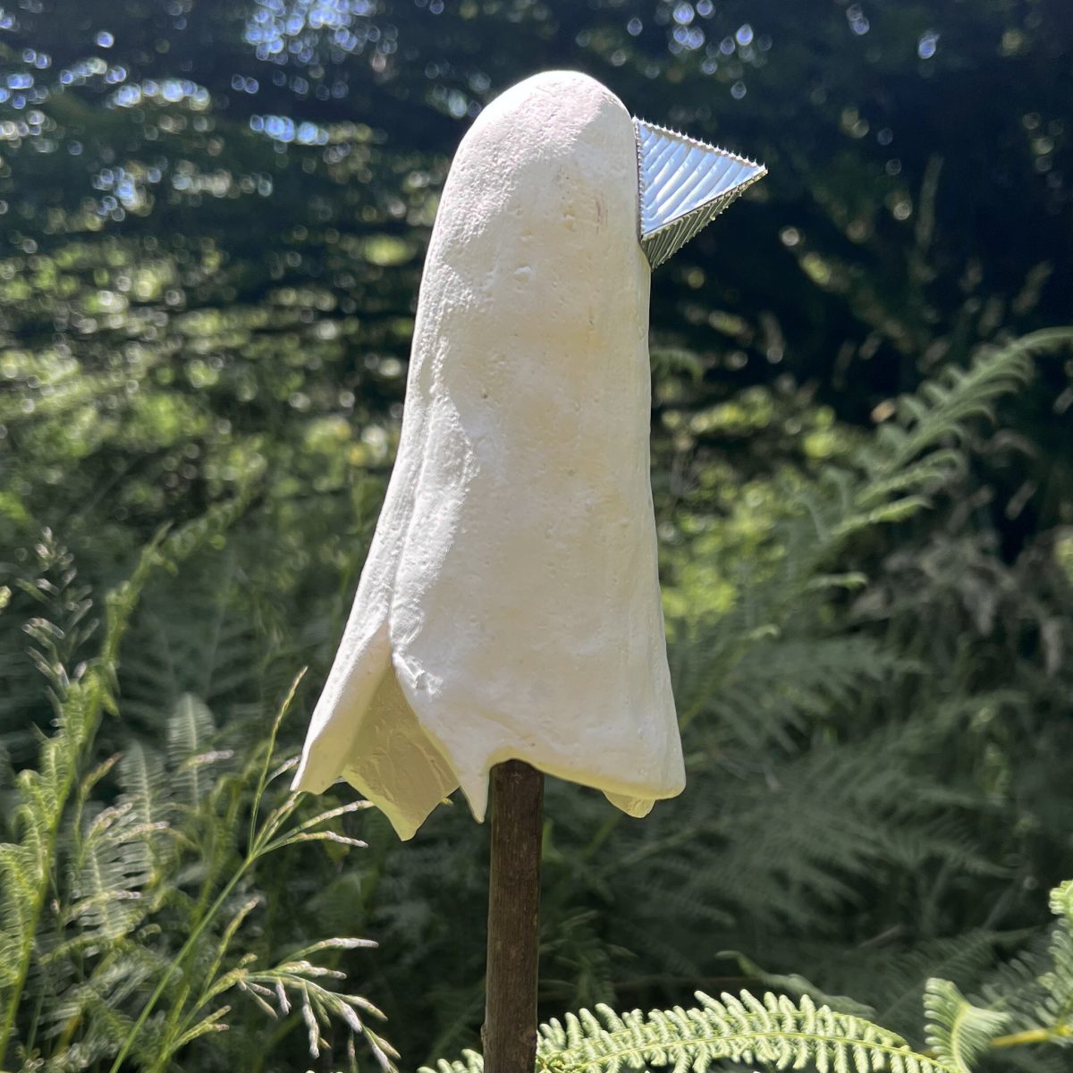 Sculpture with a matt white ceramic surface and metallic beak, outdoor setting.